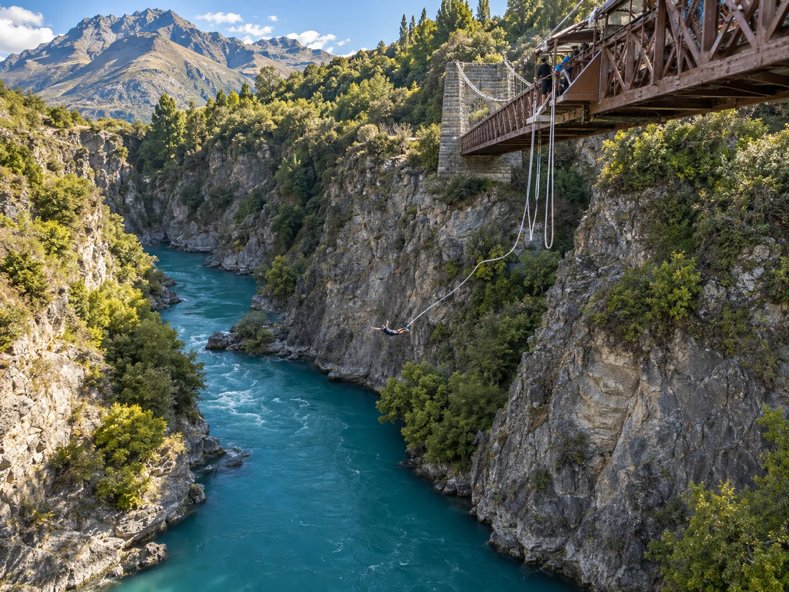 A bungy jumper mid-fall over the turquoise water of the Kawarau Gorge, viewed from the bridge above